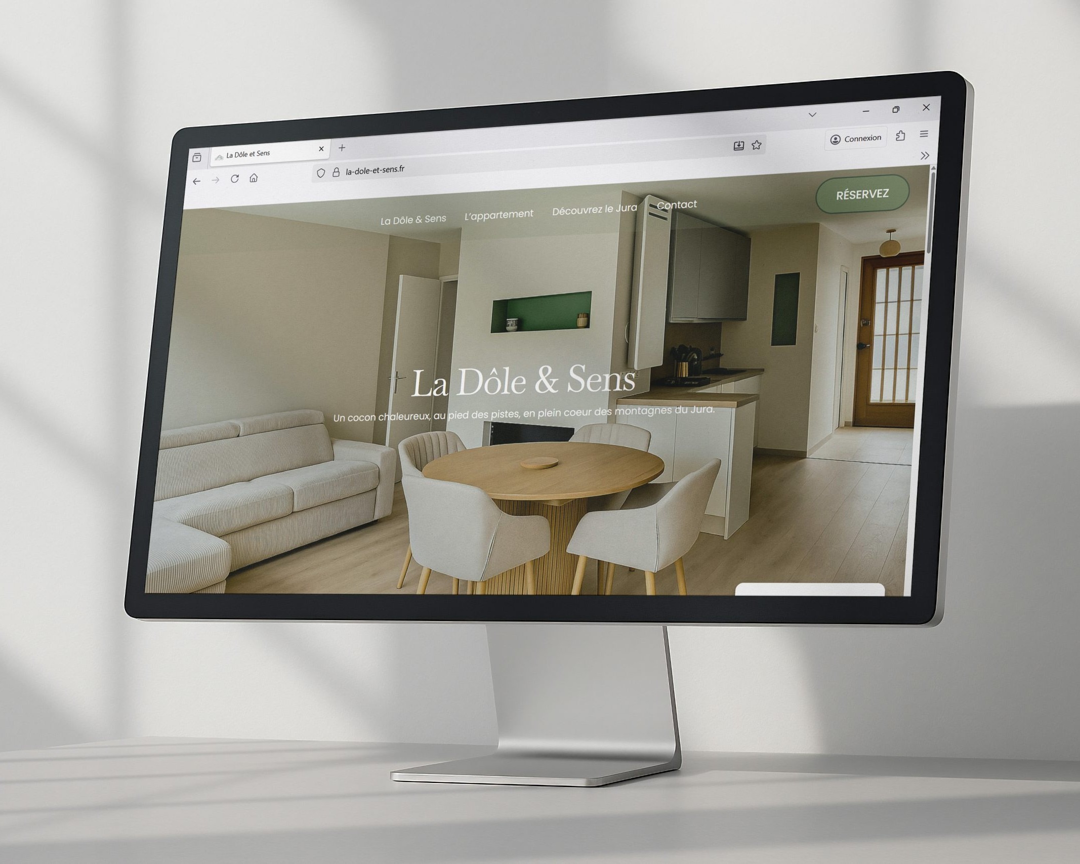 Monitor displaying a modern open-plan living space with sofa, round dining table, and kitchen in the background on a design site.
